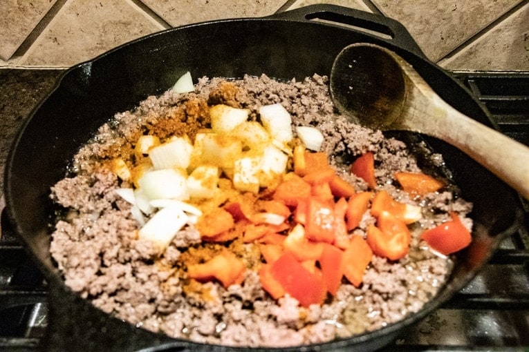 Zucchini and Ground Beef Stir Fry in a cast iron skille ton a stovetop.