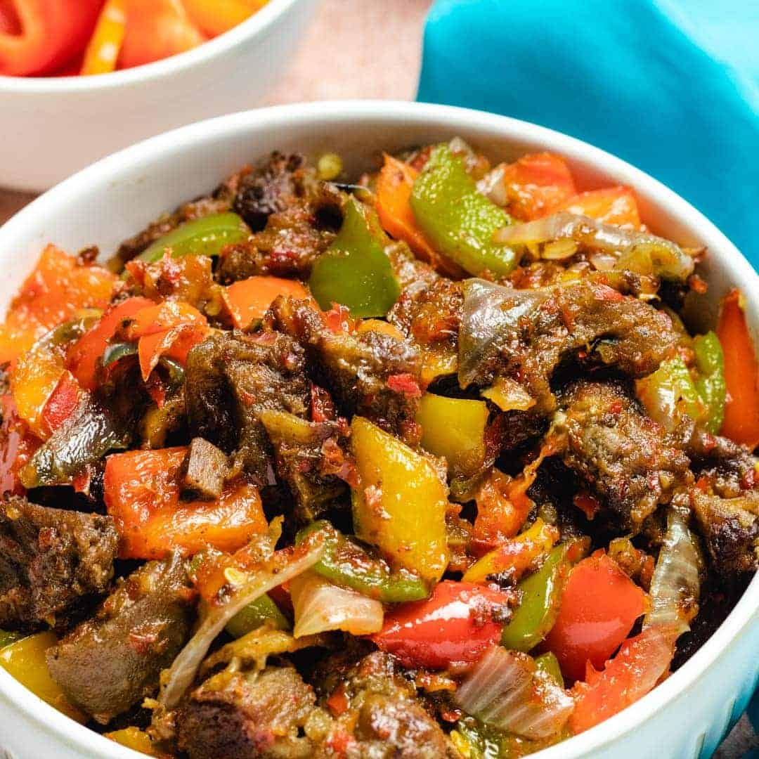 asun recipe peppered goat meat in a white dish with lots of peppers and onions.