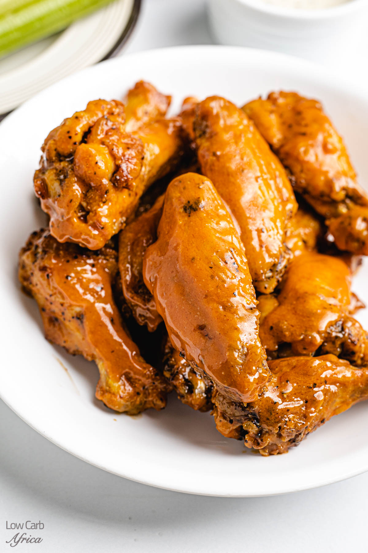 buffalo wings with celery on the side on a white plate.