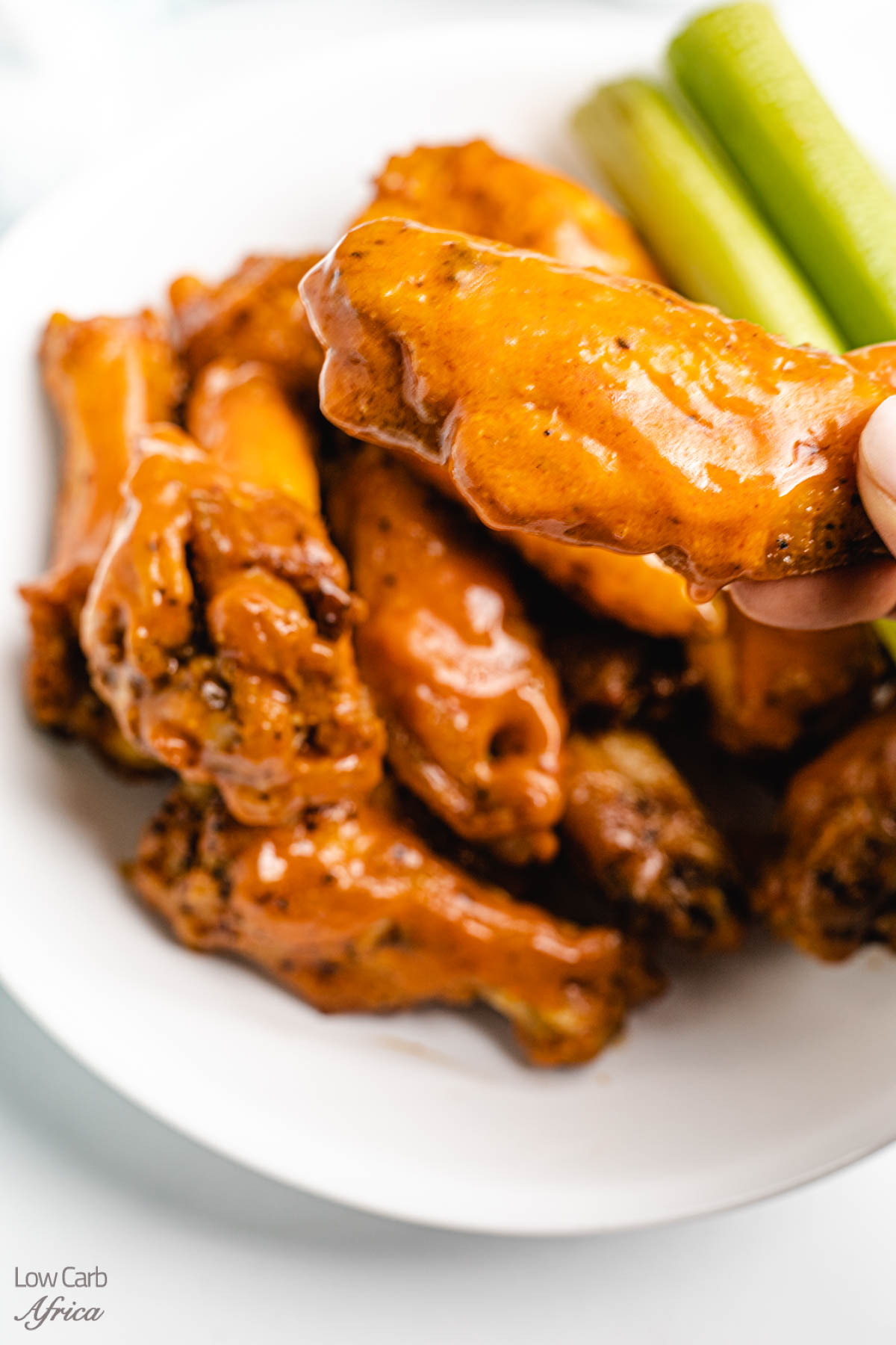 keto buffalo wings with celery on the side on a white plate.