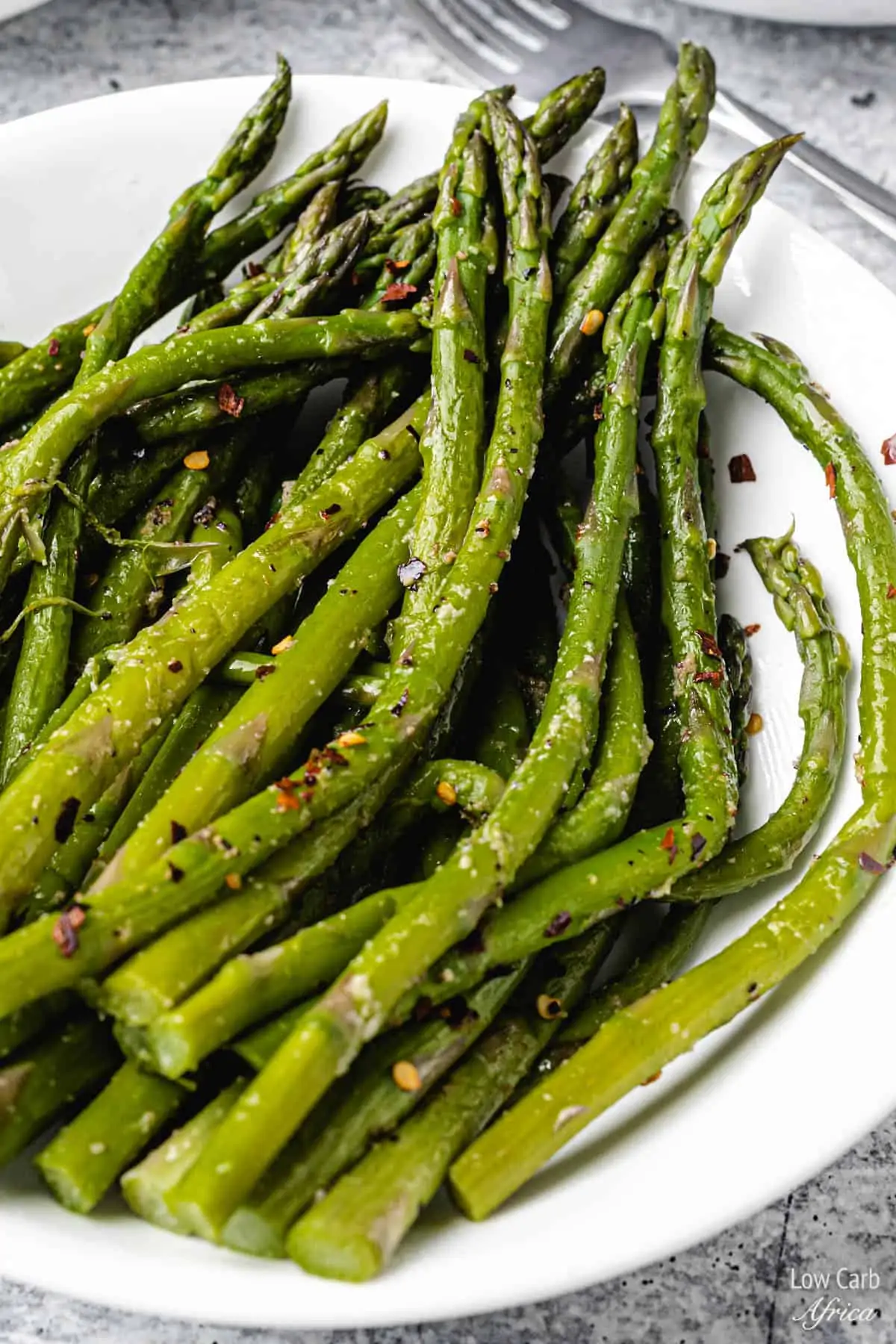 closeup shot of instant pot asparagus on a white plate with red pepper flakes.