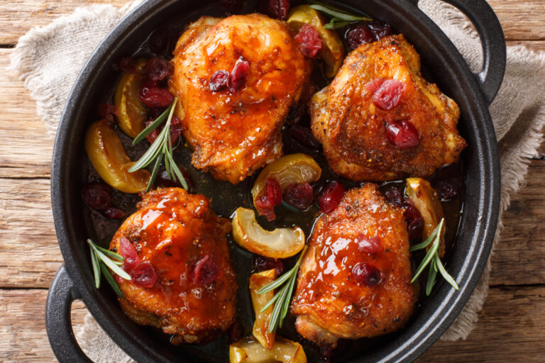 pan fried chicken thighs in a skillet with cranberries.