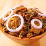 Isiewu spicy goat head on a brown bowl with sliced onions on top
